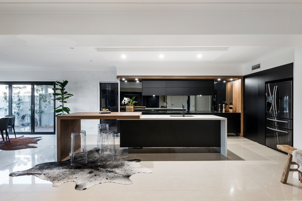 Exempel på ett modernt kök, med en undermonterad diskho, släta luckor, svarta skåp, träbänkskiva, stänkskydd med metallisk yta, spegel som stänkskydd, svarta vitvaror, en köksö och beiget golv
