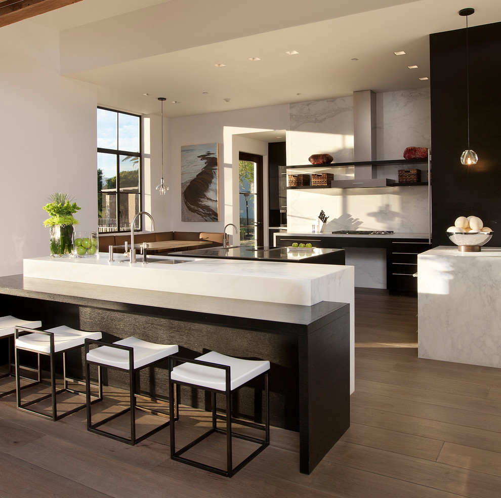 Moderne Küche mit flächenbündigen Schrankfronten, schwarzen Schränken, Küchenrückwand in Weiß, Rückwand aus Stein, dunklem Holzboden und Kücheninsel in Santa Barbara