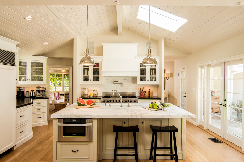 Large classic kitchen in Santa Barbara with beaded cabinets, beige cabinets, stone slab splashback, light hardwood flooring and an island.