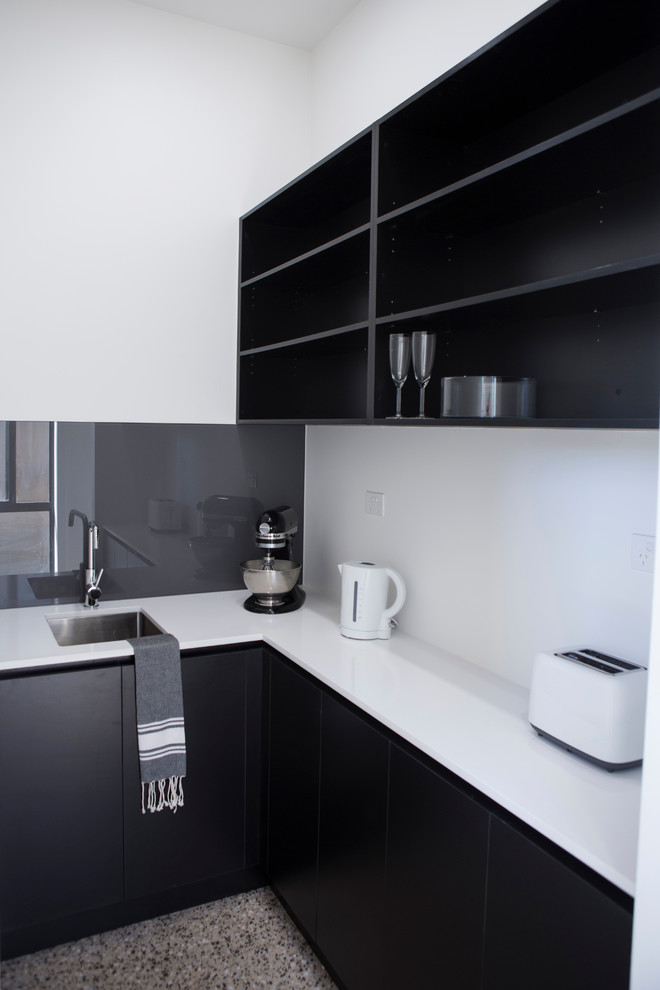 Inredning av ett modernt mellanstort kök, med svarta skåp, bänkskiva i kvarts, grått stänkskydd, glaspanel som stänkskydd, betonggolv, en enkel diskho, släta luckor och vita vitvaror