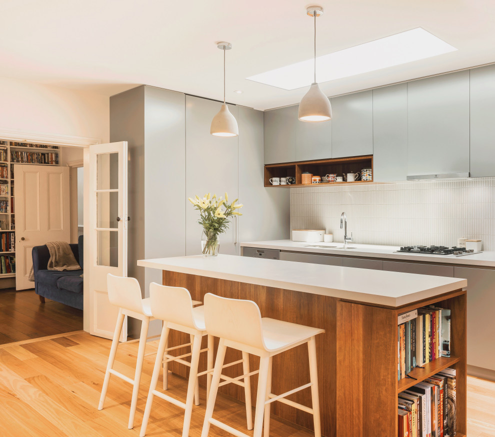 Moderne Küche mit Unterbauwaschbecken, flächenbündigen Schrankfronten, grauen Schränken, Küchenrückwand in Weiß, Rückwand aus Mosaikfliesen, hellem Holzboden, Kücheninsel, beigem Boden und weißer Arbeitsplatte in Sydney