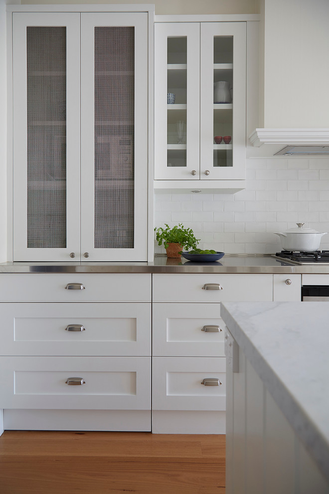 Foto på ett mellanstort vintage kök, med en undermonterad diskho, skåp i shakerstil, vita skåp, marmorbänkskiva, vitt stänkskydd, stänkskydd i porslinskakel, rostfria vitvaror, ljust trägolv och en köksö