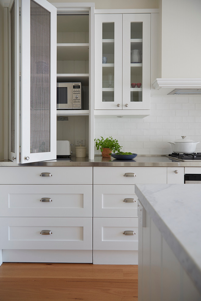 Bild på ett mellanstort vintage kök, med en undermonterad diskho, skåp i shakerstil, vita skåp, marmorbänkskiva, vitt stänkskydd, stänkskydd i porslinskakel, rostfria vitvaror, ljust trägolv och en köksö