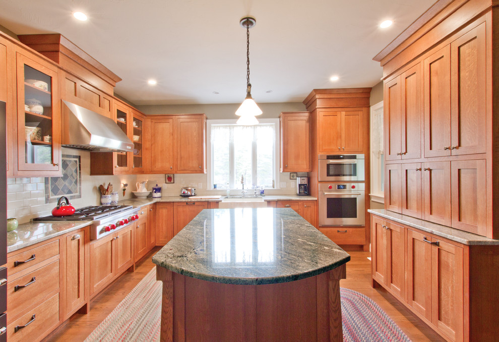 Bild på ett mellanstort amerikanskt grön grönt kök, med en rustik diskho, skåp i shakerstil, skåp i mellenmörkt trä, granitbänkskiva, vitt stänkskydd, stänkskydd i tunnelbanekakel, rostfria vitvaror, mellanmörkt trägolv, en köksö och brunt golv