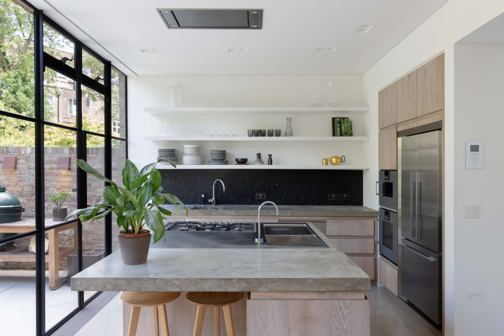 Exempel på ett modernt grå grått l-kök, med släta luckor, skåp i ljust trä, svart stänkskydd, stänkskydd i sten, rostfria vitvaror, betonggolv, en köksö och grått golv