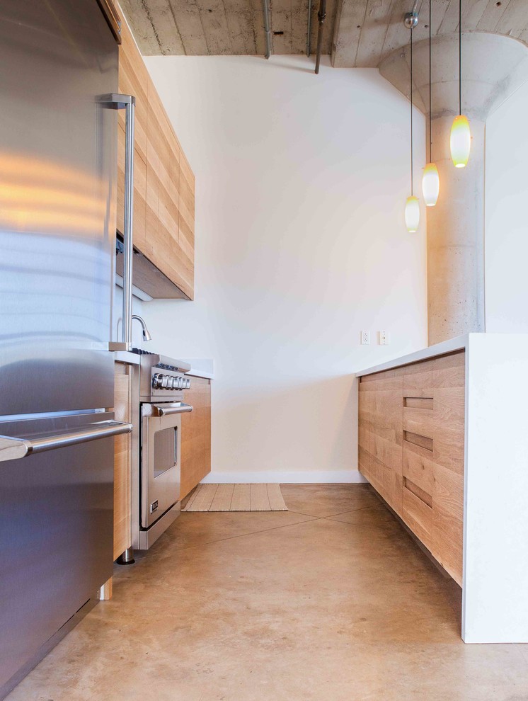 Cette photo montre une cuisine ouverte parallèle industrielle en bois brun de taille moyenne avec un placard à porte plane, une crédence blanche, un électroménager en acier inoxydable, sol en béton ciré et une péninsule.