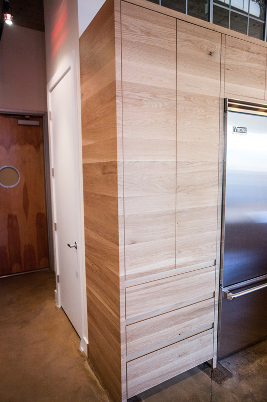 Idée de décoration pour une cuisine ouverte parallèle urbaine en bois brun de taille moyenne avec un placard à porte plane, une crédence blanche, un électroménager en acier inoxydable, sol en béton ciré et une péninsule.