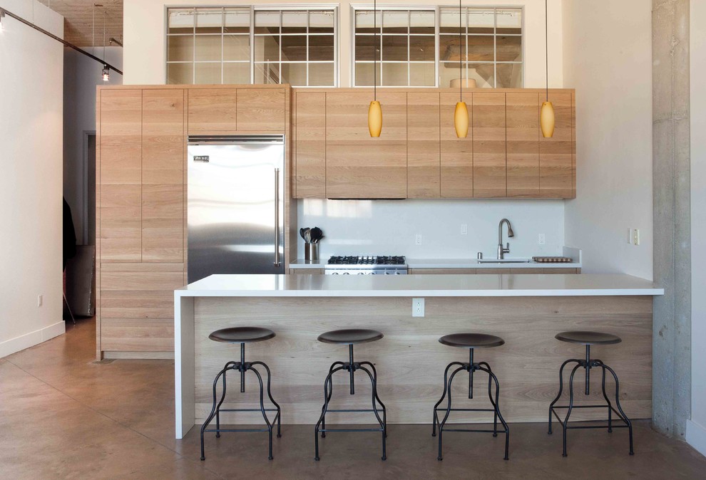 サンフランシスコにある高級な中くらいなインダストリアルスタイルのおしゃれなキッチン (フラットパネル扉のキャビネット、中間色木目調キャビネット、白いキッチンパネル、シルバーの調理設備、コンクリートの床) の写真