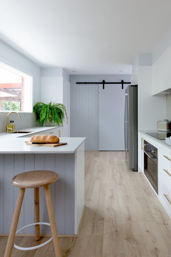 Inspiration for a country u-shaped kitchen in Sydney with a submerged sink, recessed-panel cabinets, white cabinets, stainless steel appliances, light hardwood flooring, beige floors, grey worktops and a breakfast bar.