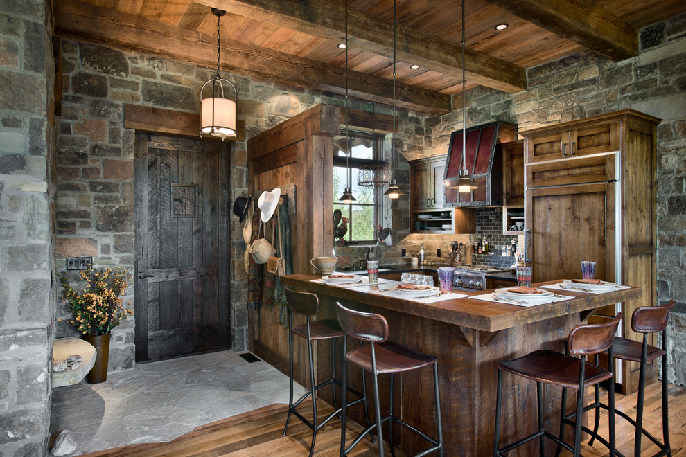 Immagine di un cucina con isola centrale stile rurale con ante in legno bruno, paraspruzzi nero, elettrodomestici da incasso e pavimento in legno massello medio