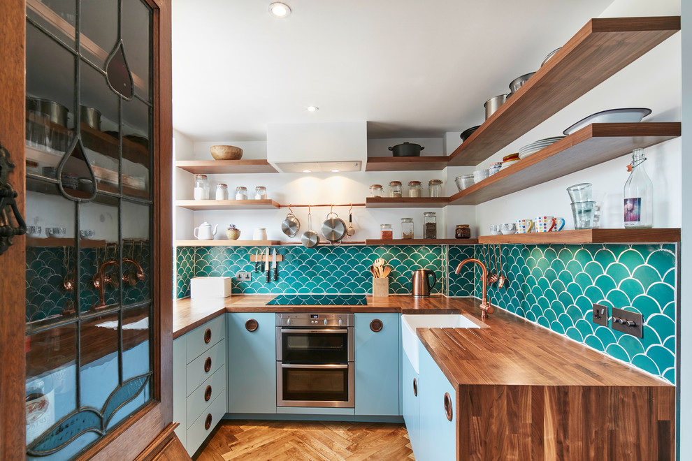 Exempel på ett avskilt, litet 60 tals u-kök, med en rustik diskho, släta luckor, blå skåp, träbänkskiva, grönt stänkskydd, stänkskydd i keramik, mellanmörkt trägolv och brunt golv