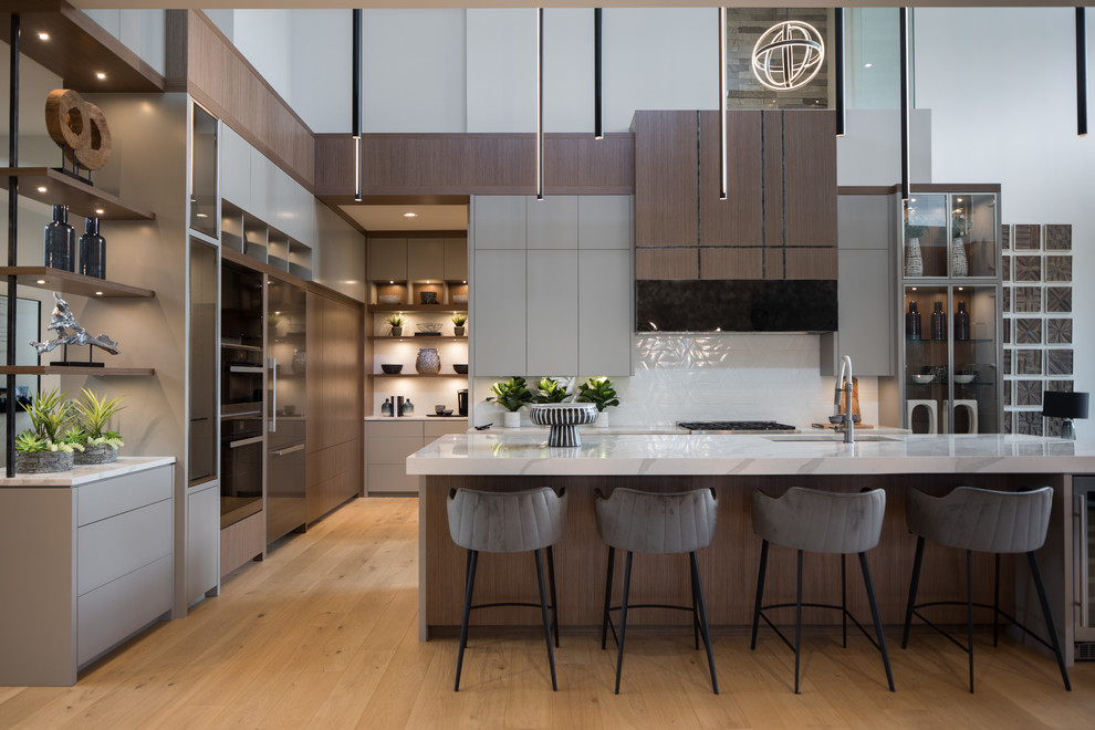 Moderne Küche in L-Form mit Unterbauwaschbecken, flächenbündigen Schrankfronten, grauen Schränken, Küchenrückwand in Weiß, Küchengeräten aus Edelstahl, braunem Holzboden, Kücheninsel, braunem Boden und weißer Arbeitsplatte in Calgary