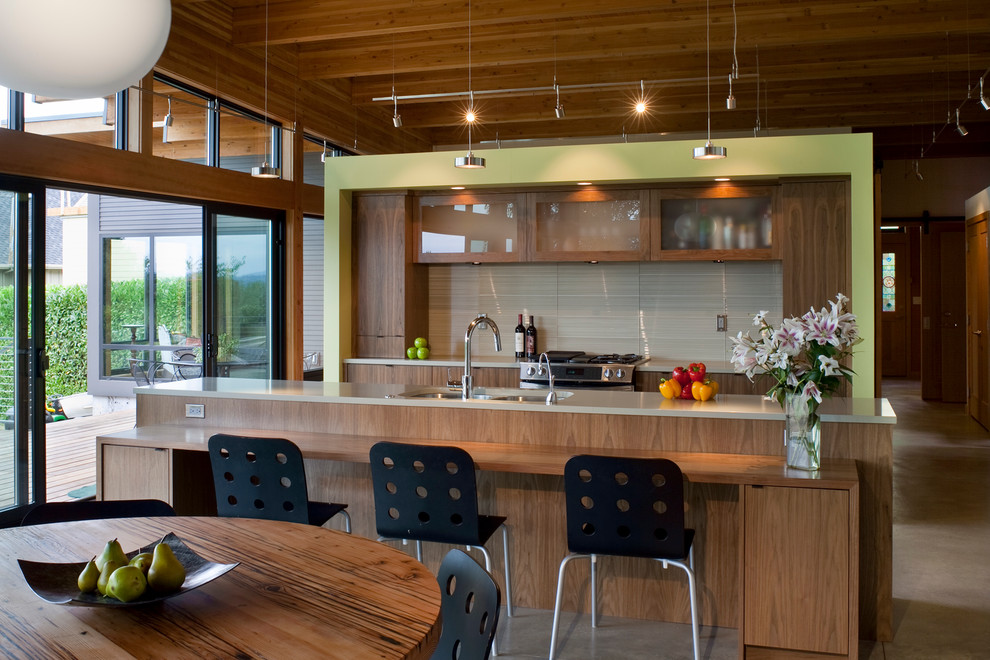 На фото: кухня в современном стиле с обеденным столом, врезной мойкой, стеклянными фасадами, фасадами цвета дерева среднего тона, серым фартуком и техникой из нержавеющей стали