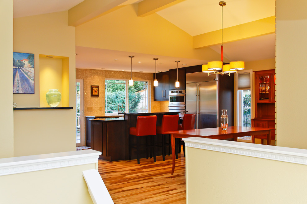 Modern inredning av ett mellanstort kök, med en undermonterad diskho, släta luckor, bruna skåp, granitbänkskiva, beige stänkskydd, stänkskydd i mosaik, rostfria vitvaror, mellanmörkt trägolv och en köksö