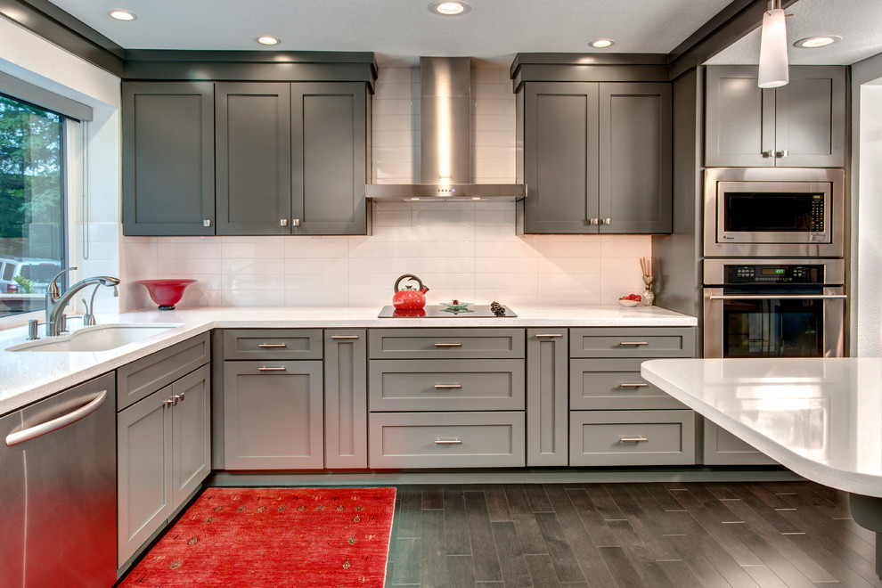 Imagen de cocina moderna de tamaño medio con fregadero bajoencimera, armarios estilo shaker, puertas de armario grises, encimera de cuarzo compacto, salpicadero blanco, electrodomésticos de acero inoxidable, suelo de madera oscura y una isla