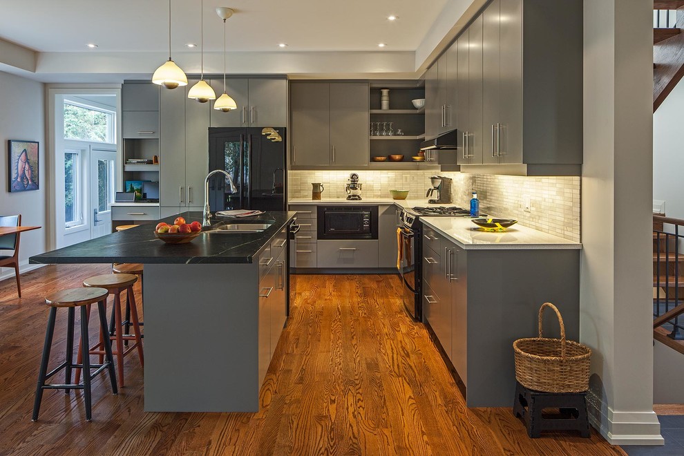 Trendy kitchen photo in Toronto with a double-bowl sink, flat-panel cabinets, gray cabinets, soapstone countertops, stone tile backsplash and white backsplash