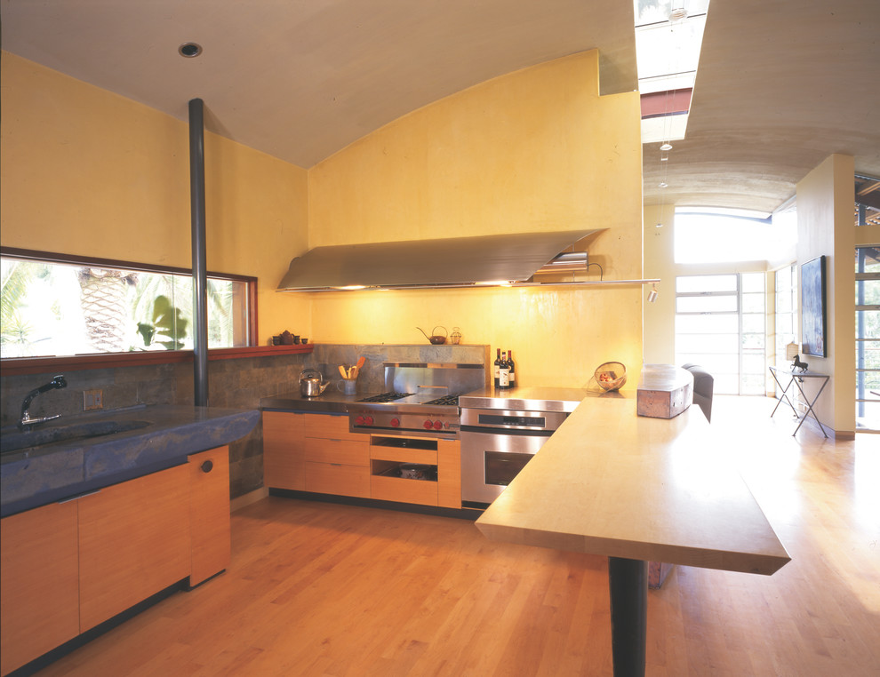 Inredning av ett modernt stort kök, med en undermonterad diskho, släta luckor, skåp i ljust trä, bänkskiva i betong, flerfärgad stänkskydd, stänkskydd i stenkakel, rostfria vitvaror och ljust trägolv