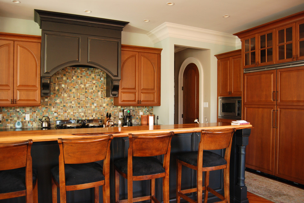 На фото: кухня в классическом стиле с фасадами с выступающей филенкой, фасадами цвета дерева среднего тона, деревянной столешницей, разноцветным фартуком, фартуком из плитки мозаики и техникой под мебельный фасад с