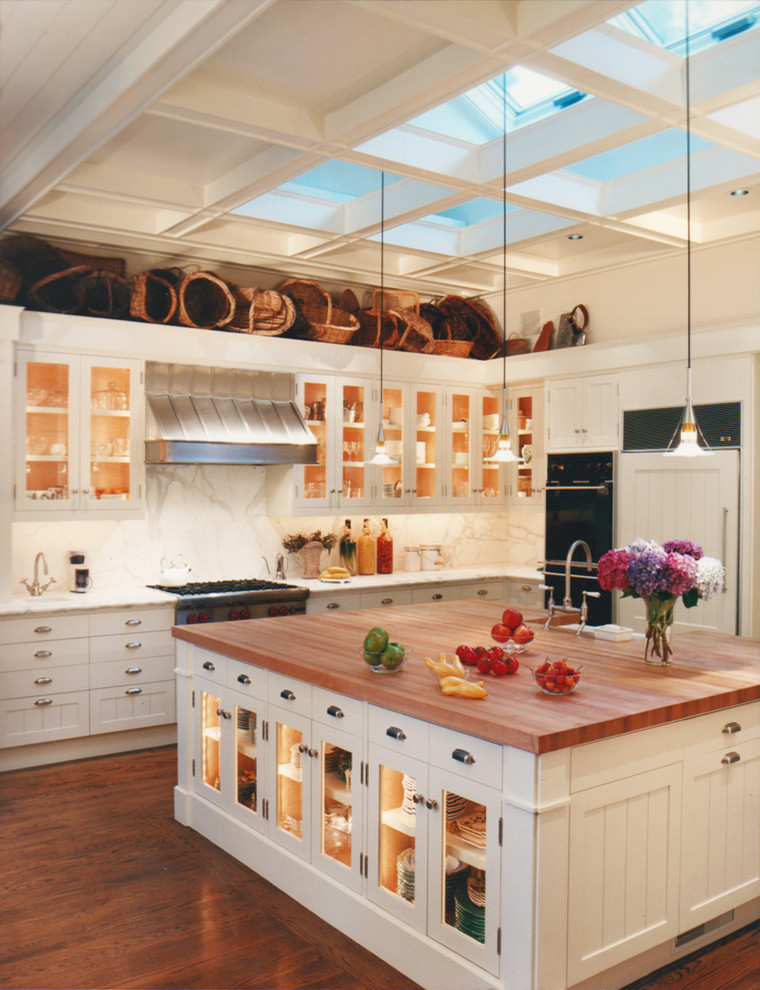 This is an example of a traditional kitchen in San Francisco with glass-front cabinets, white cabinets, white splashback, black appliances and marble splashback.