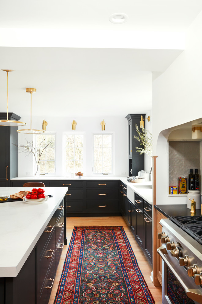 Example of a large transitional l-shaped light wood floor eat-in kitchen design in New York with a farmhouse sink, black cabinets, gray backsplash, ceramic backsplash, stainless steel appliances, an island and white countertops