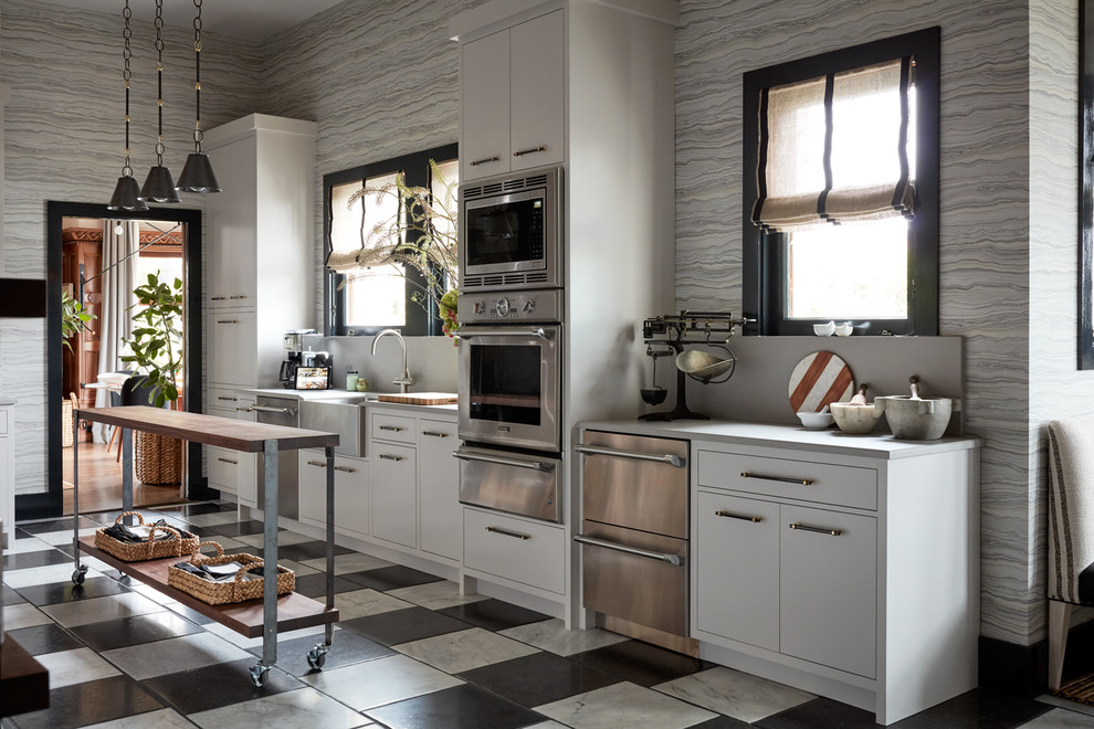 Cette image montre une cuisine parallèle design avec une crédence grise, 2 îlots, un évier de ferme, un placard à porte plane, un électroménager en acier inoxydable et un sol multicolore.