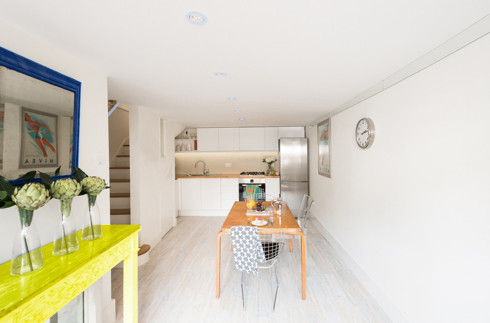 Modern inredning av ett mellanstort brun brunt kök, med en nedsänkt diskho, släta luckor, vita skåp, träbänkskiva, flerfärgad stänkskydd, stänkskydd i stenkakel, rostfria vitvaror, laminatgolv och grått golv