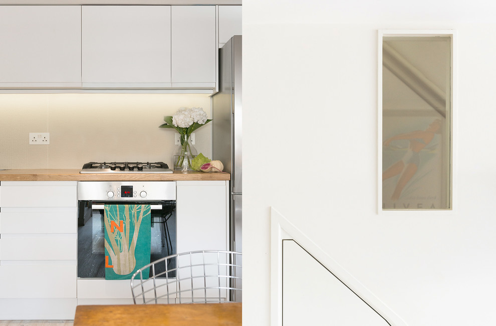 Design ideas for a small contemporary l-shaped open plan kitchen in London with a built-in sink, flat-panel cabinets, white cabinets, wood worktops, multi-coloured splashback, stone tiled splashback, stainless steel appliances, laminate floors, no island, grey floors and brown worktops.