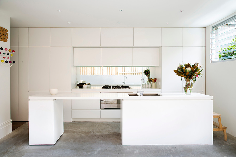 Пример оригинального дизайна: параллельная кухня в современном стиле с двойной мойкой, плоскими фасадами, белыми фасадами, техникой из нержавеющей стали, бетонным полом, островом и окном