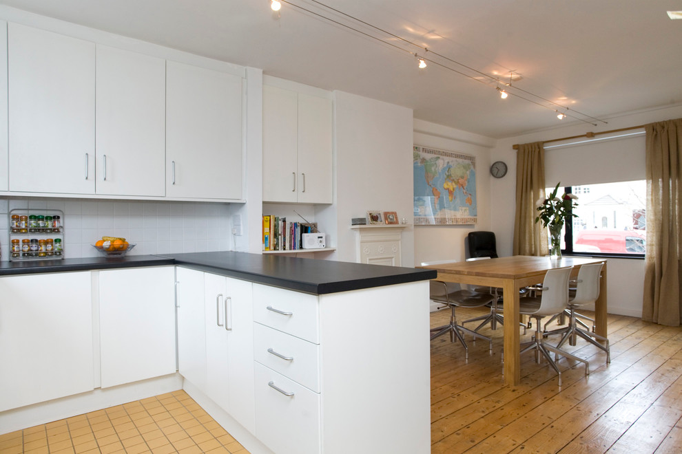 На фото: кухня в стиле модернизм с обеденным столом, плоскими фасадами, белыми фасадами и белым фартуком