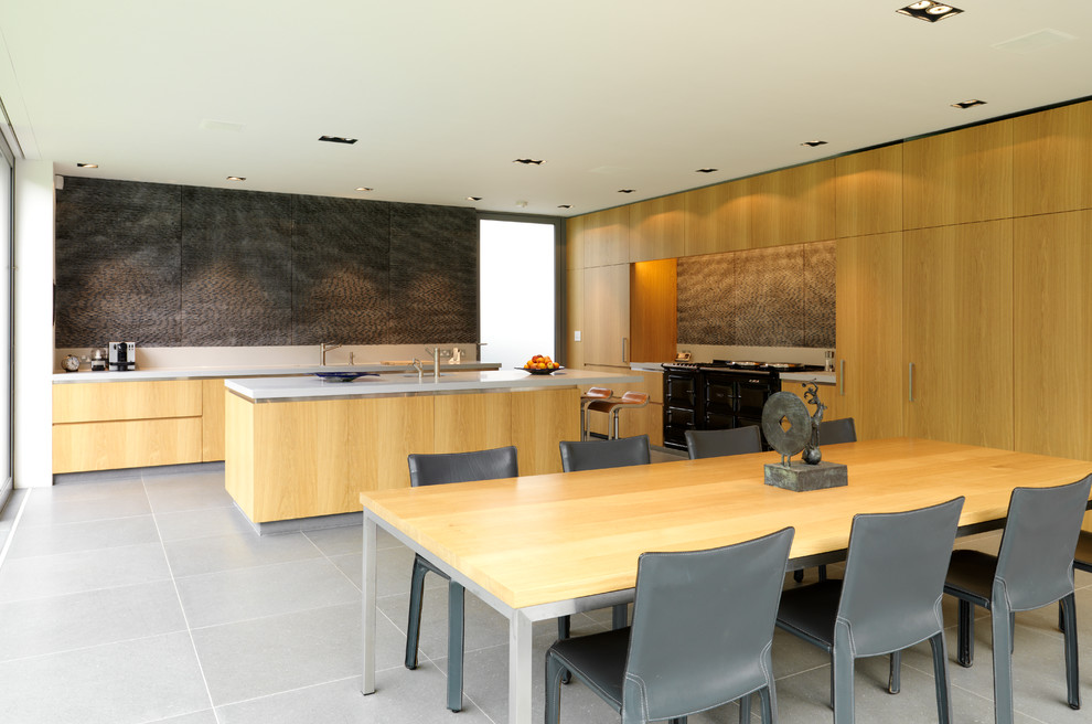 Modern l-shaped kitchen/diner in London with flat-panel cabinets, medium wood cabinets, black appliances and an island.