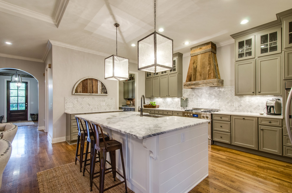 Example of a large farmhouse u-shaped medium tone wood floor open concept kitchen design in Nashville with a farmhouse sink, raised-panel cabinets, gray cabinets, marble countertops, gray backsplash, stone tile backsplash, stainless steel appliances and an island