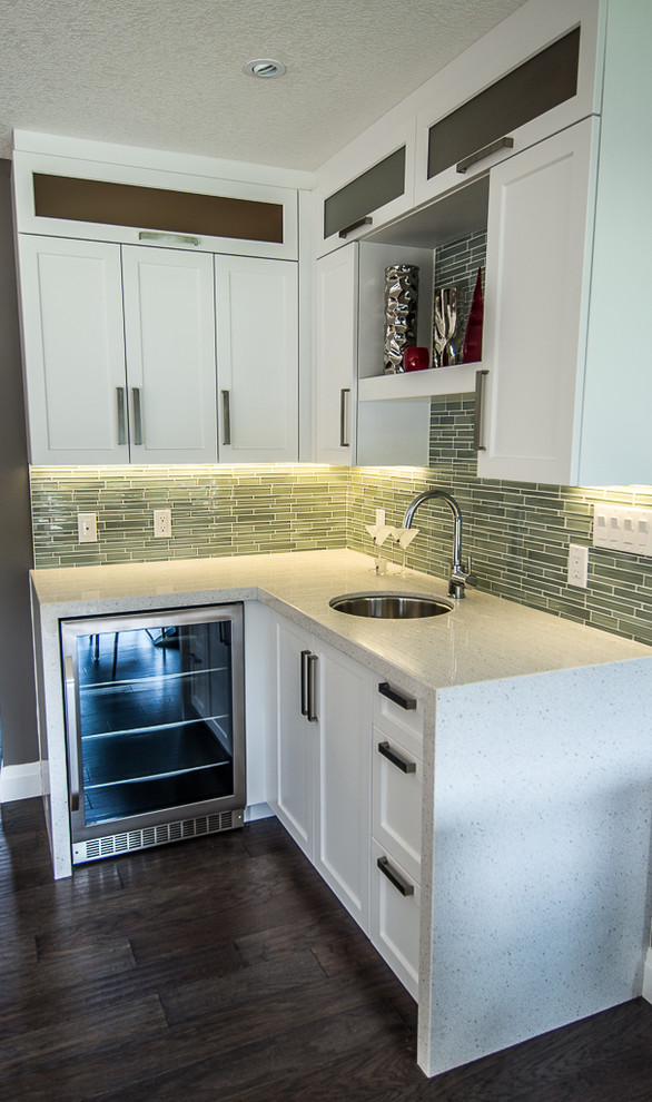 This is an example of a contemporary u-shaped kitchen/diner in Toronto with a submerged sink, shaker cabinets, white cabinets, engineered stone countertops, green splashback, glass sheet splashback and stainless steel appliances.