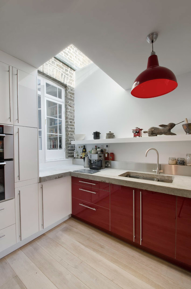 Modelo de cocina comedor lineal actual de tamaño medio con fregadero de doble seno, puertas de armario rojas, encimera de cemento, salpicadero metalizado y electrodomésticos de acero inoxidable