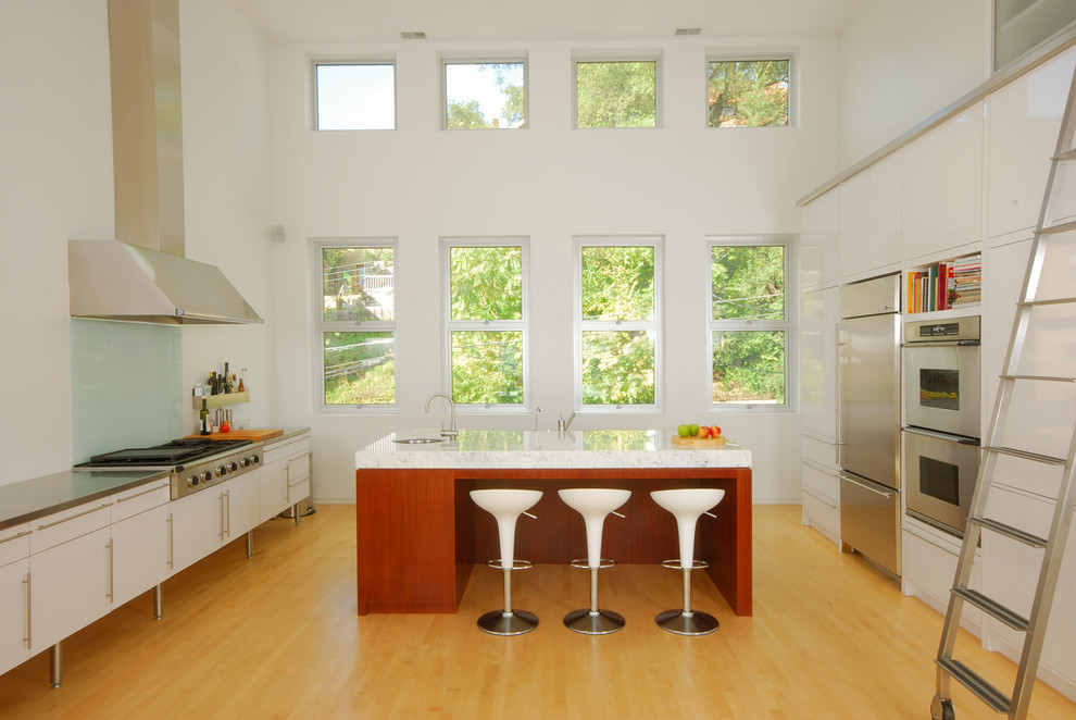 Große Moderne Küche mit flächenbündigen Schrankfronten, weißen Schränken, Küchengeräten aus Edelstahl, hellem Holzboden und Kücheninsel in Cincinnati