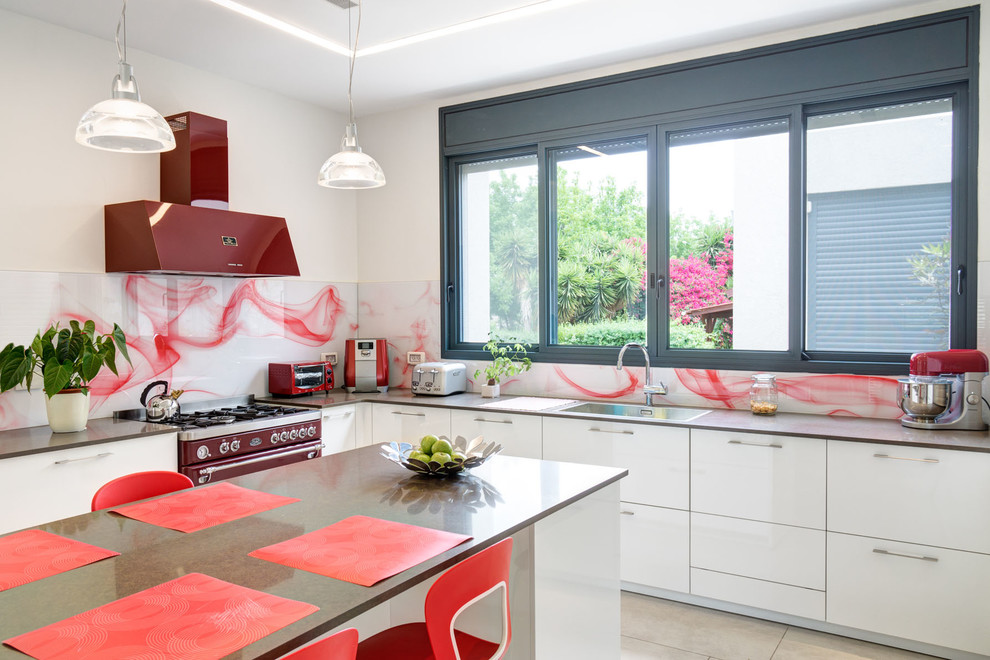На фото: большая п-образная кухня в стиле модернизм с плоскими фасадами, белыми фасадами, красным фартуком, фартуком из стекла, цветной техникой и полом из керамической плитки
