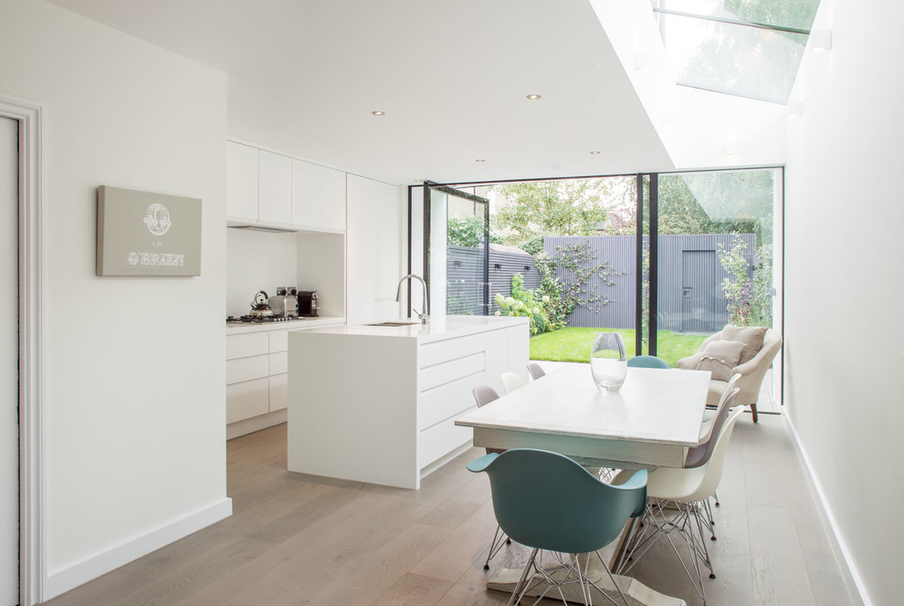 Contemporary kitchen/diner in London with a submerged sink, flat-panel cabinets, white cabinets, white splashback, glass sheet splashback, medium hardwood flooring, an island, stainless steel appliances, brown floors and white worktops.