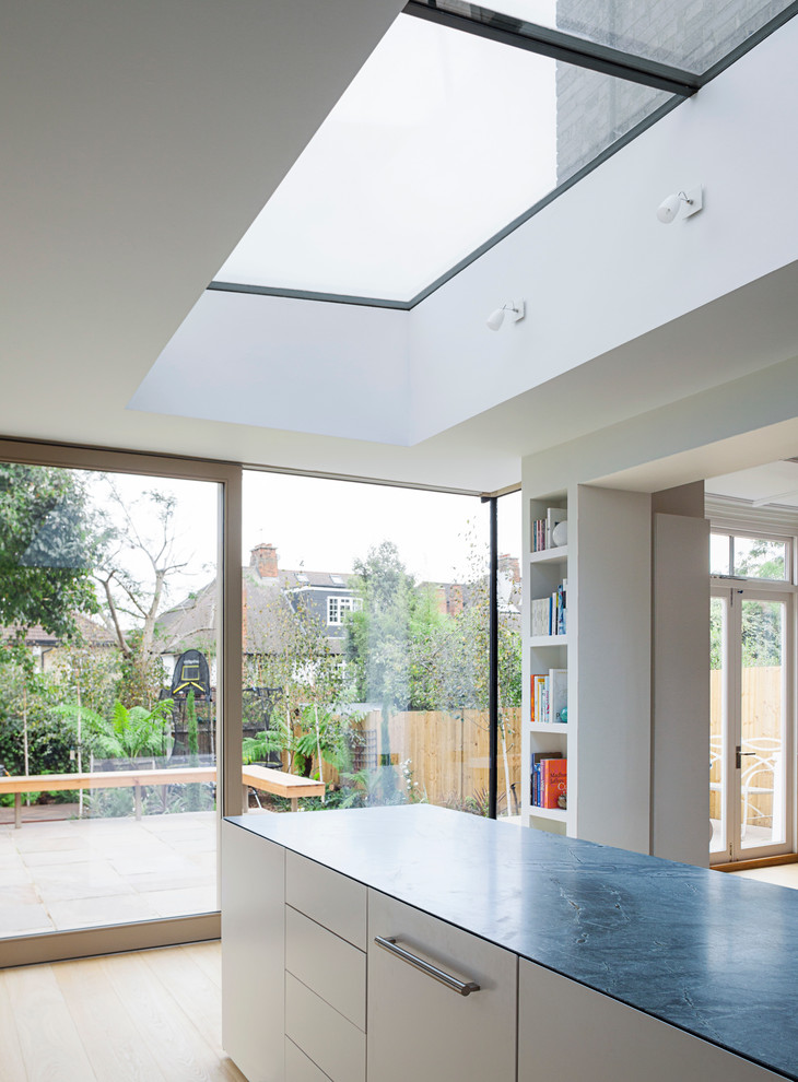Photo of a large contemporary l-shaped open plan kitchen in London with a built-in sink, flat-panel cabinets, white cabinets, marble worktops, grey splashback, stone slab splashback, stainless steel appliances, light hardwood flooring and an island.