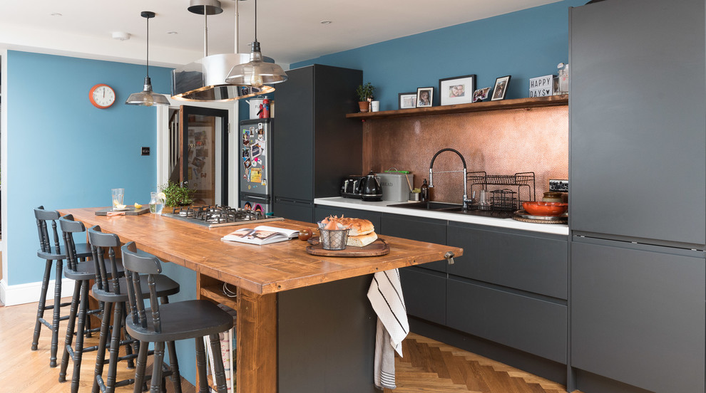 Mittelgroße, Zweizeilige Moderne Küchenbar mit flächenbündigen Schrankfronten, grauen Schränken, Kücheninsel, braunem Boden, Küchenrückwand in Metallic und braunem Holzboden in London