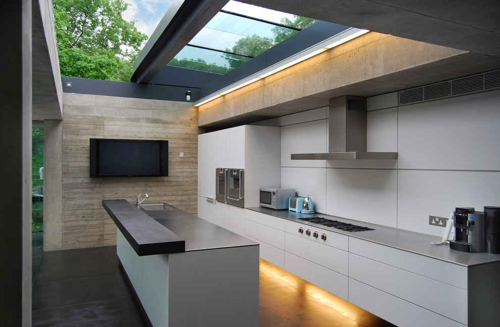 Mid-sized trendy single-wall eat-in kitchen photo in London with a drop-in sink, flat-panel cabinets, white cabinets, stainless steel countertops, white backsplash, paneled appliances and an island