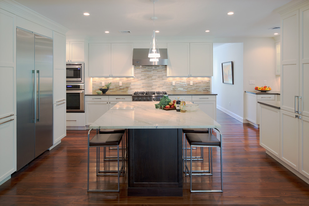 Inspiration for a mid-sized transitional u-shaped medium tone wood floor eat-in kitchen remodel in New York with shaker cabinets, white cabinets, granite countertops, white backsplash, glass tile backsplash, stainless steel appliances and an island