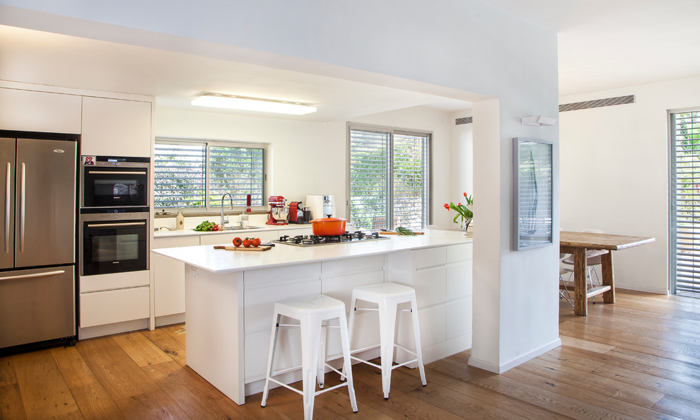 This is an example of a contemporary open plan kitchen in Other with flat-panel cabinets, white cabinets and an island.