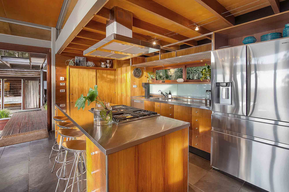 シドニーにあるトロピカルスタイルのおしゃれなアイランドキッチン (一体型シンク、フラットパネル扉のキャビネット、中間色木目調キャビネット、ステンレスカウンター、シルバーの調理設備、グレーの床) の写真