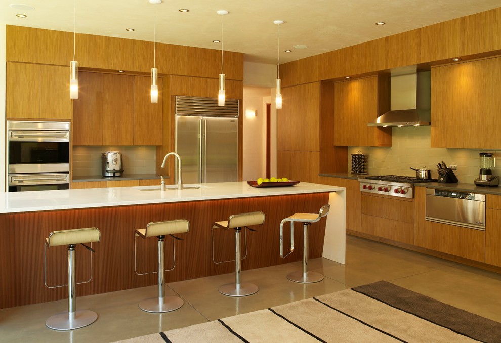 Cette image montre une cuisine design en L et bois brun avec un placard à porte plane, une crédence beige, un électroménager en acier inoxydable, sol en béton ciré et îlot.