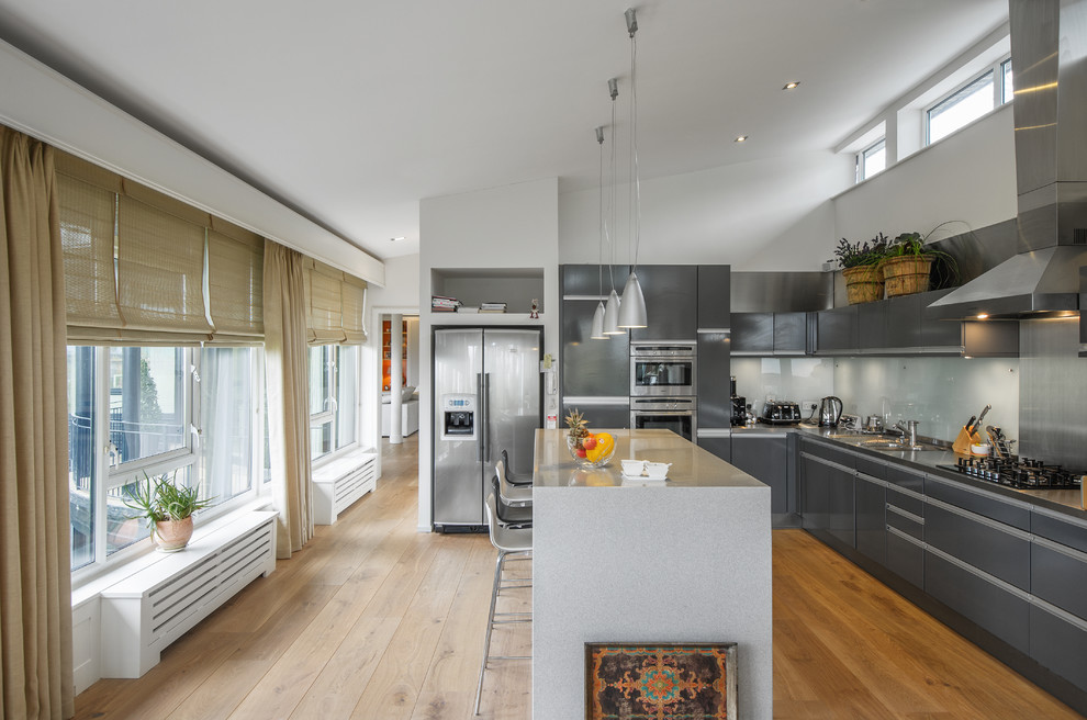 Medium sized contemporary l-shaped kitchen in Dublin with flat-panel cabinets, grey cabinets, white splashback, glass sheet splashback, stainless steel appliances and an island.