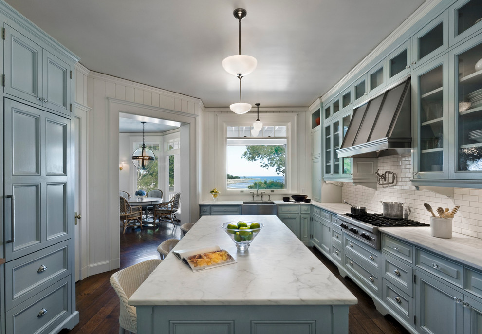 Example of a beach style dark wood floor kitchen design in New York with glass-front cabinets, blue cabinets, white backsplash, subway tile backsplash, stainless steel appliances and an island