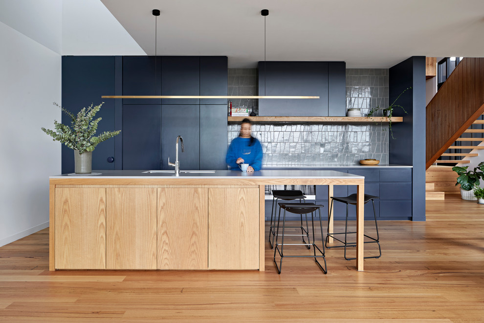 Idéer för stora funkis grått kök, med en dubbel diskho, släta luckor, blå skåp, bänkskiva i kvarts, grått stänkskydd, stänkskydd i keramik, svarta vitvaror, ljust trägolv och en köksö