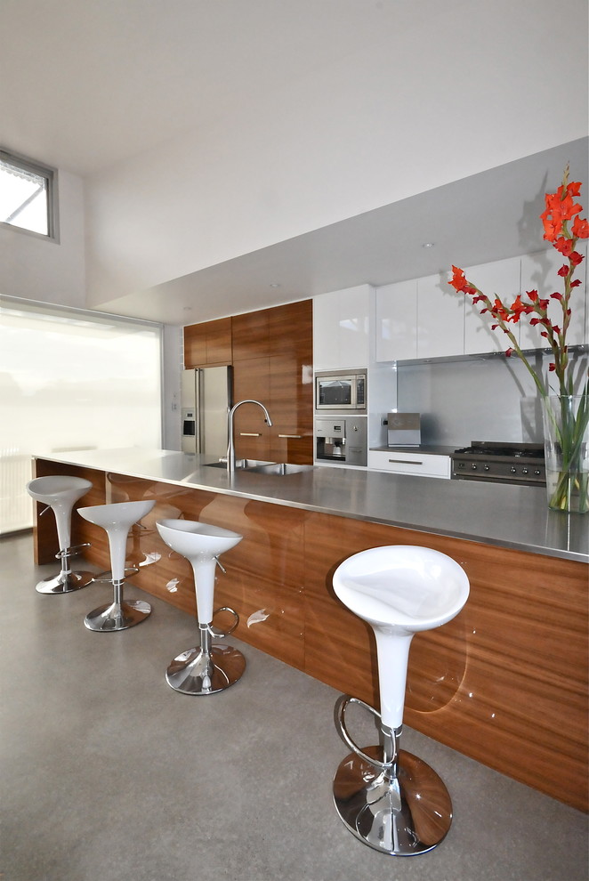 Exempel på ett mellanstort modernt kök, med en integrerad diskho, skåp i mellenmörkt trä, bänkskiva i rostfritt stål, stänkskydd med metallisk yta, rostfria vitvaror, betonggolv och en köksö