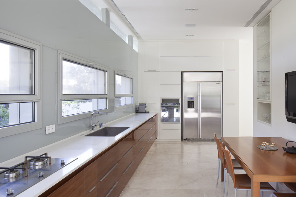 Photo of an expansive modern single-wall enclosed kitchen in Tel Aviv with stainless steel appliances, a submerged sink, flat-panel cabinets, medium wood cabinets, engineered stone countertops, grey splashback, glass sheet splashback, limestone flooring and no island.