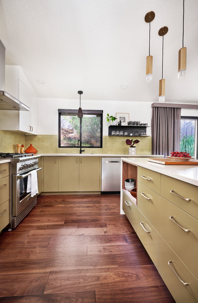 Foto på ett mellanstort eklektiskt beige kök, med en undermonterad diskho, släta luckor, gröna skåp, bänkskiva i kvarts, grönt stänkskydd, stänkskydd i porslinskakel, rostfria vitvaror, mellanmörkt trägolv, en halv köksö och brunt golv