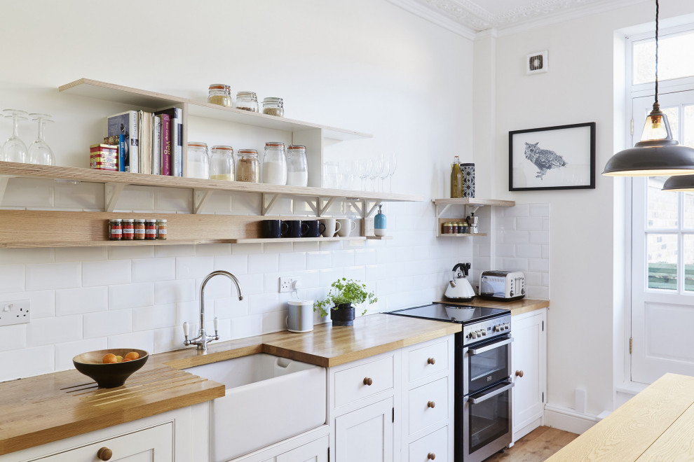 Mittelgroße Nordische Küche mit Landhausspüle, weißen Schränken, Arbeitsplatte aus Holz, Küchenrückwand in Weiß, braunem Holzboden, Kassettenfronten und Rückwand aus Metrofliesen in London
